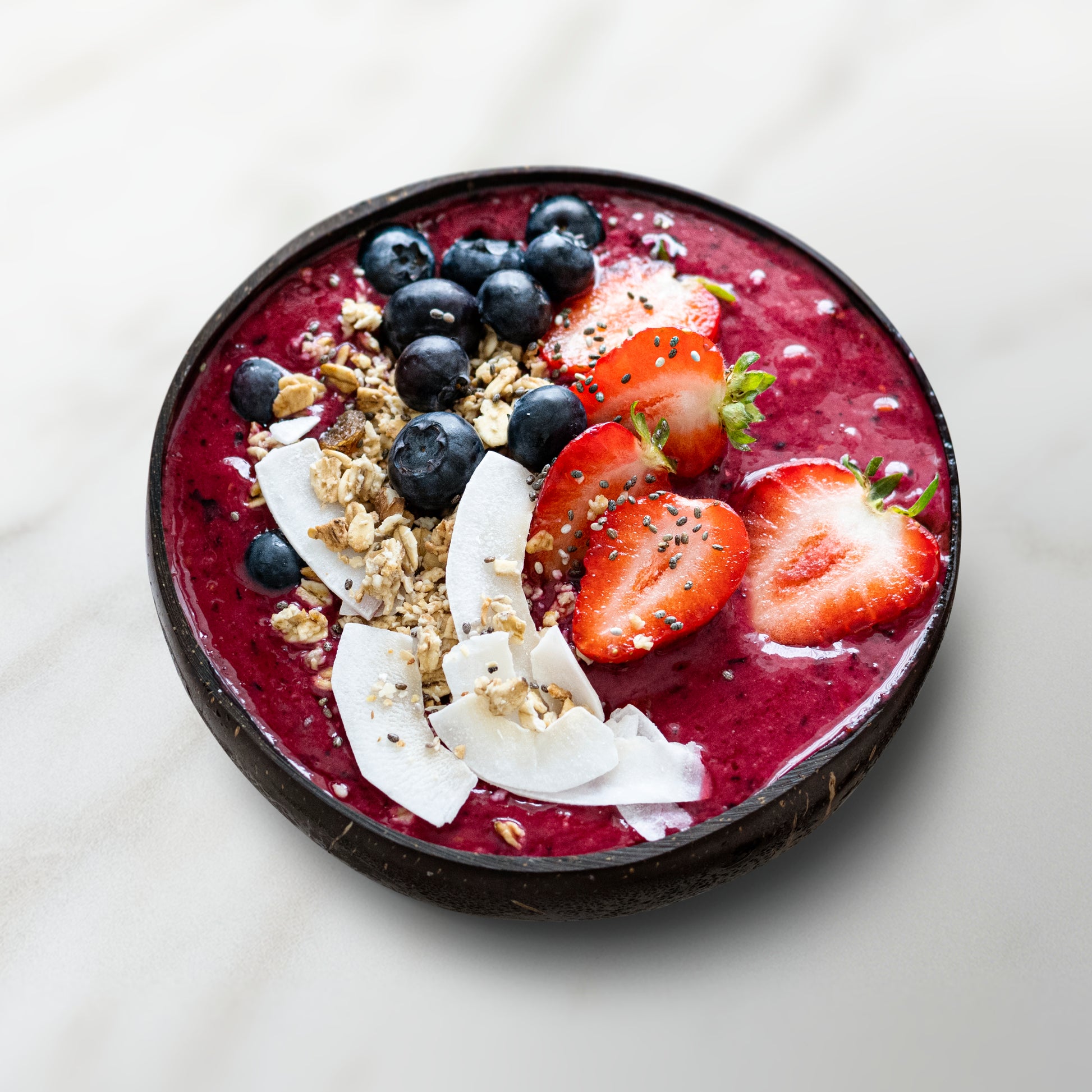 smoothie bowl avec un smoothie rouge, fraise, myrtilles, noix de coco et céréales