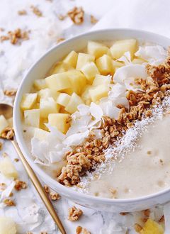 Smoothie bowl avec un smoothie jaune, des morceau de pomme, noix de coco, graines et céréales